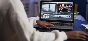 Editor de vídeo trabalhando em seu laptop com um software de edição, ajustando clipes na linha do tempo